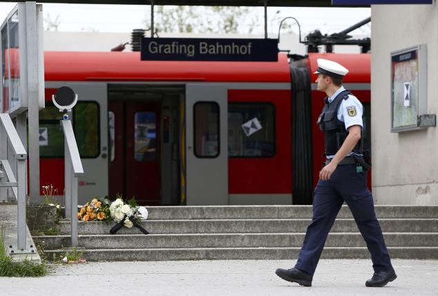 A policeman walks past flowers, placed at the stairs of a train station, following a knife attack in Grafing train station