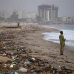 A man stands on the shore of Bar Beach, awash with rubbish and waste, in Lagos