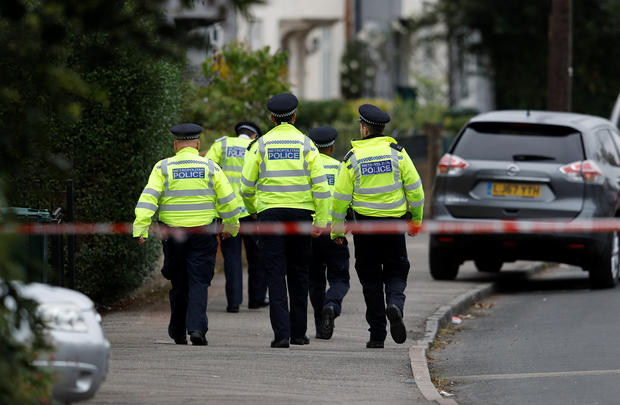 Police officers walk behind cordon tape set up around a property being searched after a man was arrested in connection with an explosion on a London Underground train, in Sunbury-on-Thames