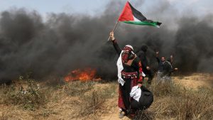 Woman demonstrator holds a Palestinian flag during clashes with Israeli troops at a protest where Palestinians demand the right to return to their homeland, at the Israel-Gaza border in the southern Gaza Strip