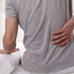 Man suffering from back pain at home in the bedroom. Uncomfortable mattress and pillow causes back pain.