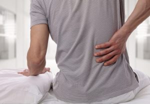 Man suffering from back pain at home in the bedroom. Uncomfortable mattress and pillow causes back pain.