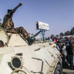 A-sudanese-soldier-gives-the-power-salute-as-protesters-mass-around-the-defense-ministry-complex-e1554965720507