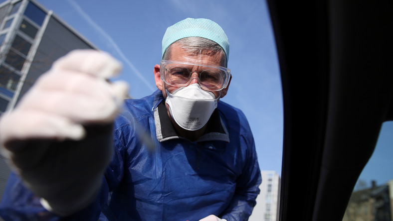 German doctor Michael Grosse takes a sample from a car driver through the window on March 27, 2020 at a drive through testing point for the novel coronavirus on a parking in Halle, eastern Germany. (Photo by Ronny Hartmann / AFP)