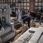 SPAIN: A priest and relatives pray as a COVID-19 victim’s coffin is buried at the Almudena cemetery in Madrid.(Olmo Calvo/Associated Press)