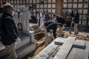 SPAIN: A priest and relatives pray as a COVID-19 victim’s coffin is buried at the Almudena cemetery in Madrid.(Olmo Calvo/Associated Press)
