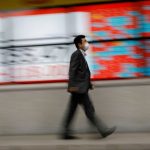 A man wearing a protective face mask, following the coronavirus disease (COVID-19) outbreak, walks in front of a stock quotation board outside a brokerage in Tokyo