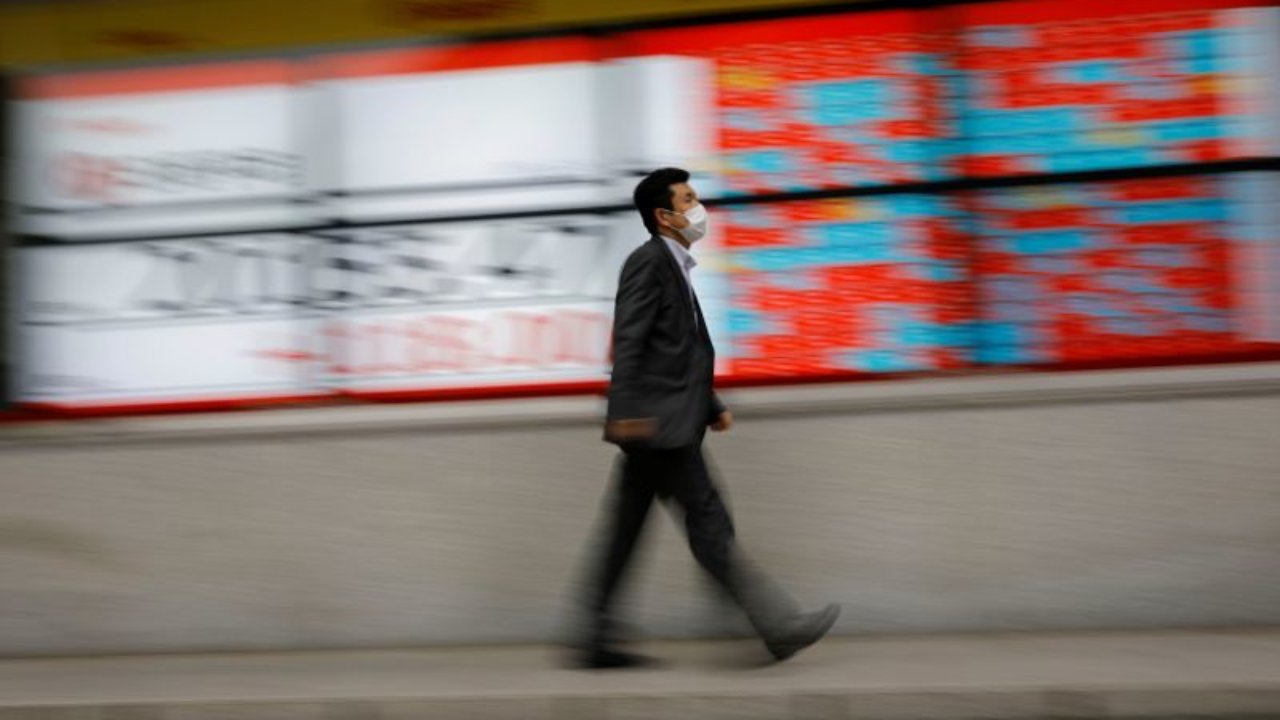 A man wearing a protective face mask, following the coronavirus disease (COVID-19) outbreak, walks in front of a stock quotation board outside a brokerage in Tokyo