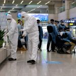 Workers wearing protective gear disinfect an arrival gate as other workers check passengers from overseas upon their arrival at the Incheon International Airport, in Incheon