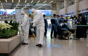 Workers wearing protective gear disinfect an arrival gate as other workers check passengers from overseas upon their arrival at the Incheon International Airport, in Incheon