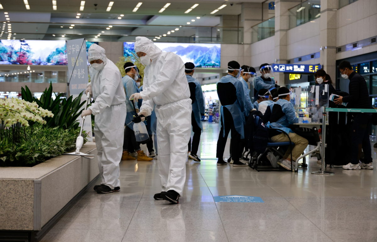 Workers wearing protective gear disinfect an arrival gate as other workers check passengers from overseas upon their arrival at the Incheon International Airport, in Incheon