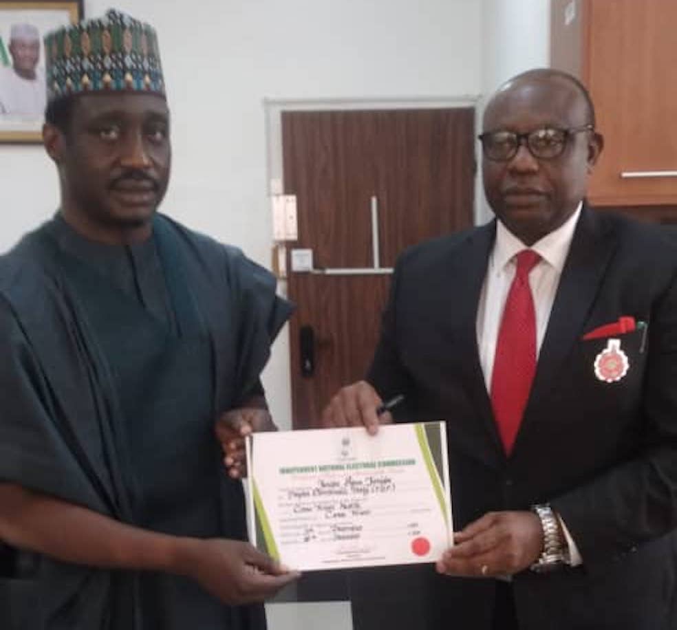 Rt Hon Jarigbe, left, receiving the CoR from Festis Okoye, right, INEC Commissioner in charge of Information and Voter Education