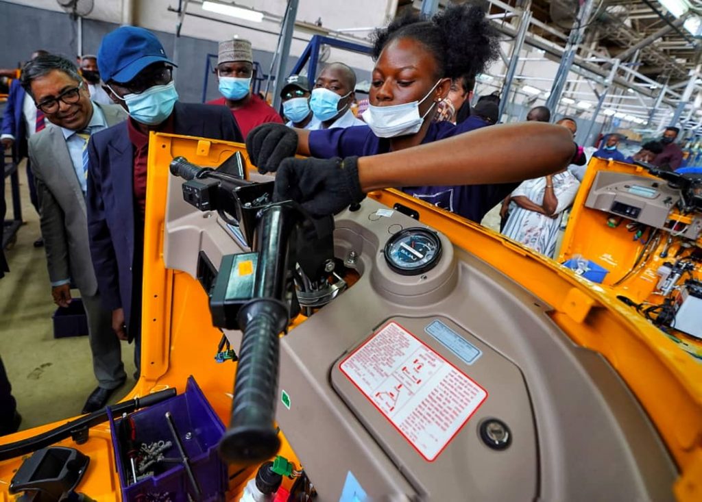 Gov.Babajide Sanwo-Olu of Lagos watches as a female technician contributes to assembling a Bajaj tricycle in Lagos
