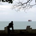 a-man-sitting-on-a-bench-next-to-a-body-of-water-the-gulf-of-guinea-is-the-most-dangerous-sea-in-the_224978_