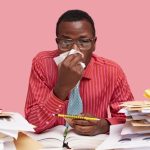 sick-black-male-worker-has-running-nose-uses-tissue-works-coworking-space-holds-spiral-notepad-with-pencil-has-finish-work-isolated-pink-space_273609-23685