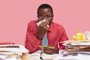 sick-black-male-worker-has-running-nose-uses-tissue-works-coworking-space-holds-spiral-notepad-with-pencil-has-finish-work-isolated-pink-space_273609-23685