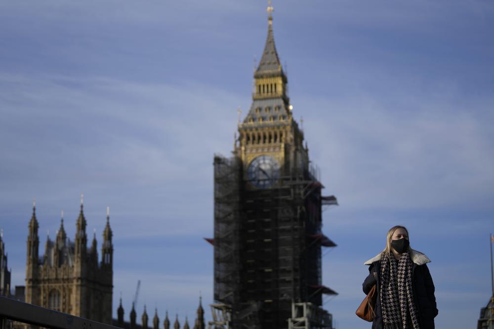 A woman wears a face mask as she crosses Westminster Bridge in London, Thursday, Dec. 9, 2021. British Prime Minister Boris Johnson has announced tighter restrictions to stem the spread of the omicron variant. He is again urging people to work from home and mandating COVID-19 passes to get into nightclubs and large events. (AP Photo/Frank Augstein)