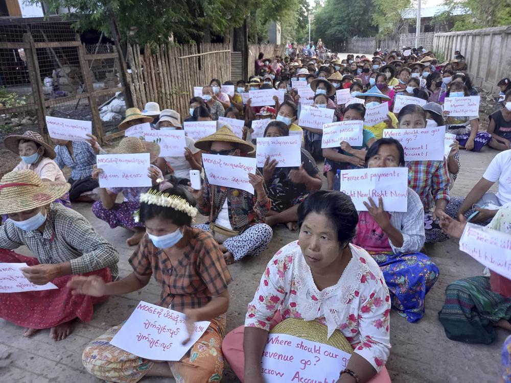 In this photo provided by Nwe Oo Tawlanyae Latpantaung, women sit in protest in the village of Latpantaung in Myanmar on Oct. 28, 2021, while holding signs in English and Burmese calling for the freezing of revenues the Myanmar military gets from the sale of oil and gas. As the military’s abuses have grown after seizing power in February, people from Myanmar’s southern jungles to its northern mountains are voicing support for targeted sanctions on oil and gas funds, the country’s single largest source of foreign currency revenue. (Courtesy of Nwe Oo Tawlanyae Latpantaung via AP)