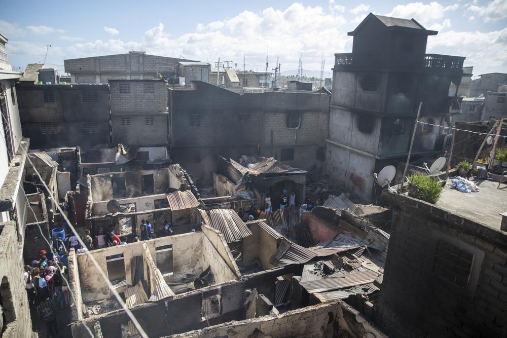 Residents stand amid their homes damaged by a gasoline truck that overturned and exploded in Cap-Haitien, Haiti, Tuesday, Dec. 14, 2021. The explosion engulfed cars and homes in flames, killing more than 50 people and injuring dozens of others. (AP Photo/Joseph Odelyn)