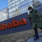 A woman wearing a face mask run past the offices of Chinese e-commerce firm Alibaba in Beijing on Dec. 13, 2021. A former employee of Chinese e-commerce giant Alibaba says human resources and upper management wouldn’t deal with her accusation of sexual assault. So she went into the busy cafeteria at the headquarters of the Chinese e-commerce giant and screamed out her plight. Now she is paying the price. The company fired her. (AP Photo/Andy Wong)