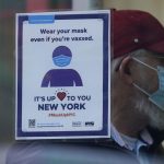 FILE – A sign reminds customers that masks are required in their store in New York, Dec. 13, 2021. The new omicron coronavirus mutant speeding around the world may bring another wave of chaos, threatening to further stretch hospital workers already struggling with a surge of delta cases and upend holiday plans for the second year in a row. (AP Photo/Seth Wenig, File)