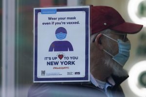 FILE – A sign reminds customers that masks are required in their store in New York, Dec. 13, 2021. The new omicron coronavirus mutant speeding around the world may bring another wave of chaos, threatening to further stretch hospital workers already struggling with a surge of delta cases and upend holiday plans for the second year in a row. (AP Photo/Seth Wenig, File)