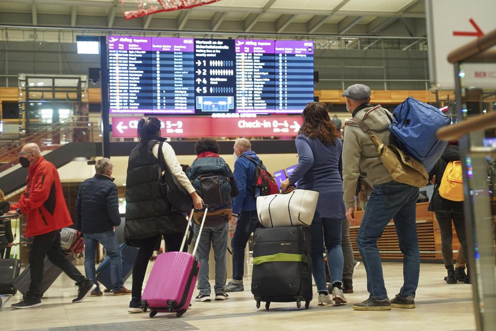 Travellers stand in front of an information board at BER Airport in Berlin, Germany, Saturday, Dec. 18, 2021. Germany’s incoming transport minister is advising people against traveling over Christmas as the country tries to stem a wave of coronavirus infections. (Joerg Carstensen/dpa via AP)