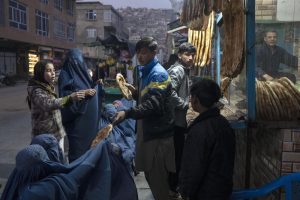 FILE – A man distributes bread to Burka-wearing Afghan women outside a bakery in Kabul, Afghanistan, Thursday, Dec, 2, 2021. Pakistan is rallying Muslim countries to help Afghanistan stave off an economic and humanitarian disaster while also cajoling the neighboring country’s new Taliban rulers into concessions to soften their image abroad. (AP Photo/Petros Giannakouris, File)