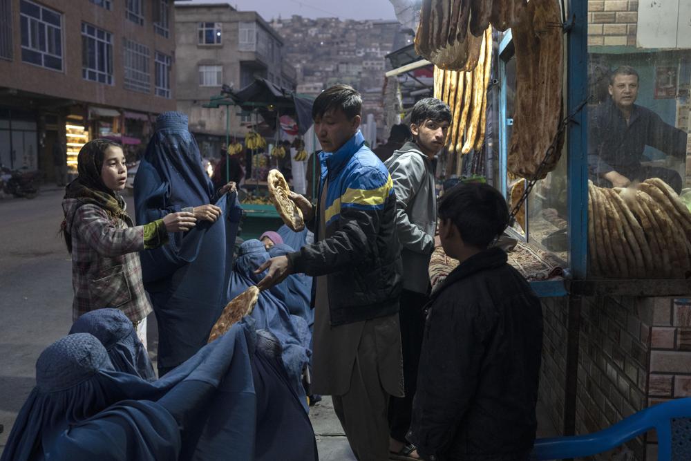 FILE – A man distributes bread to Burka-wearing Afghan women outside a bakery in Kabul, Afghanistan, Thursday, Dec, 2, 2021. Pakistan is rallying Muslim countries to help Afghanistan stave off an economic and humanitarian disaster while also cajoling the neighboring country’s new Taliban rulers into concessions to soften their image abroad. (AP Photo/Petros Giannakouris, File)