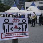 Social distancing signs on precautions against the coronavirus are displayed as people queue in line for the coronavirus testing at a public health center in Seoul, South Korea, Thursday, Dec. 9, 2021. New coronavirus infections in South Korea have been rising and breaking records daily. There were long lines at testing stations after they exceeded 7,000 for the first time on Wednesday since the start of the pandemic. More than 5,600 of the new 7,175 cases were reported in Seoul and the nearby metropolitan region. (AP Photo/Ahn Young-joon)