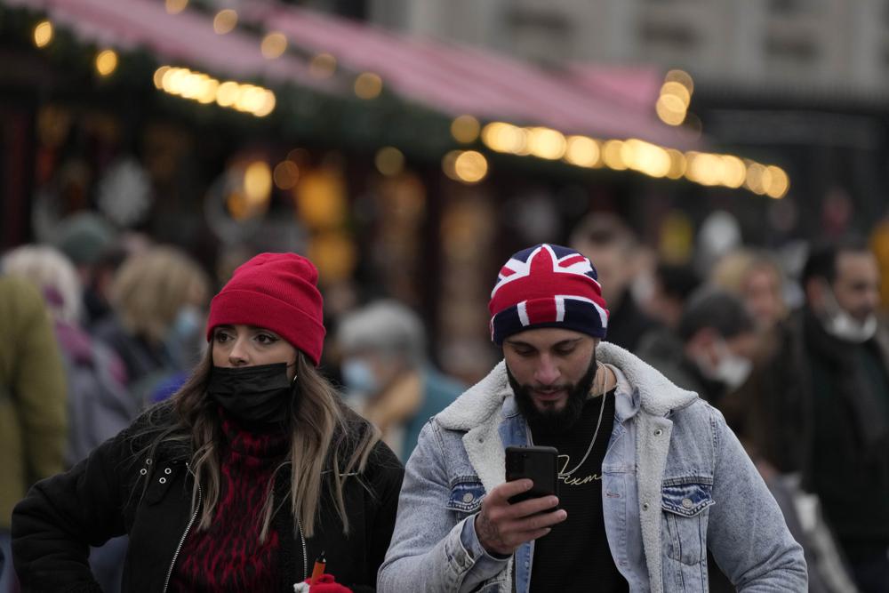 People walk past a Christmas market in Trafalgar Square in London, Wednesday, Dec. 22, 2021. British Prime Minister Boris Johnson said on Monday that his government reserves the “possibility of taking further action” to protect public health as Omicron spreads across the country. (AP Photo/Frank Augstein)