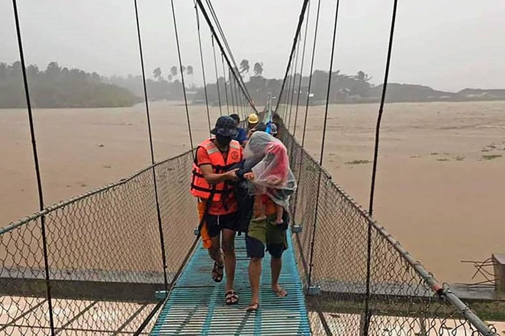 In this handout photo provided by the Philippine Coast Guard, rescuers assist residents cross a bridge as they are evacuated to higher grounds in Tubay town, Agusan del Norte, southern Philippines on Thursday, Dec. 16, 2021. Tens of thousands of people were being evacuated to safety in the southern and central Philippines as Typhoon Rai approached Thursday at a time when authorities were warning the public to avoid crowds after the first infections caused by the omicron strain of the coronavirus were reported in the country, officials said. (Philippine Coast Guard via AP)
