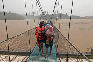 In this handout photo provided by the Philippine Coast Guard, rescuers assist residents cross a bridge as they are evacuated to higher grounds in Tubay town, Agusan del Norte, southern Philippines on Thursday, Dec. 16, 2021. Tens of thousands of people were being evacuated to safety in the southern and central Philippines as Typhoon Rai approached Thursday at a time when authorities were warning the public to avoid crowds after the first infections caused by the omicron strain of the coronavirus were reported in the country, officials said. (Philippine Coast Guard via AP)