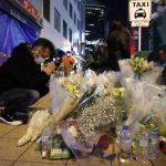 A mourner prays in front of offerings near a building where a fire broke out, in Osaka, western Japan Saturday, Dec. 18, 2021. Japanese police on Sunday identified a 61-year-old man as a prime arson suspect after a fire engulfed a mental clinic in the eight-story building where he was a patient, killing more than 20 people who were trapped inside. (Kyodo News via AP)