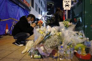 A mourner prays in front of offerings near a building where a fire broke out, in Osaka, western Japan Saturday, Dec. 18, 2021. Japanese police on Sunday identified a 61-year-old man as a prime arson suspect after a fire engulfed a mental clinic in the eight-story building where he was a patient, killing more than 20 people who were trapped inside. (Kyodo News via AP)