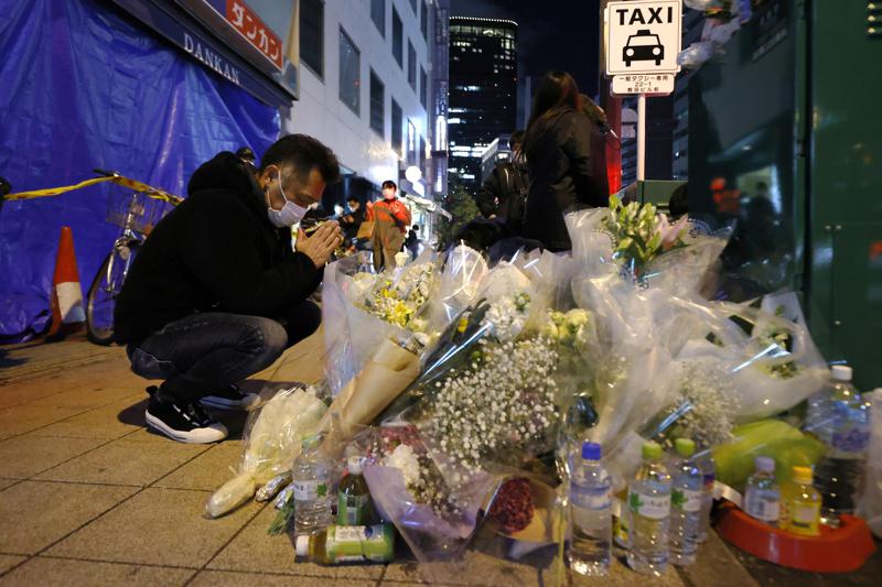 A mourner prays in front of offerings near a building where a fire broke out, in Osaka, western Japan Saturday, Dec. 18, 2021. Japanese police on Sunday identified a 61-year-old man as a prime arson suspect after a fire engulfed a mental clinic in the eight-story building where he was a patient, killing more than 20 people who were trapped inside. (Kyodo News via AP)