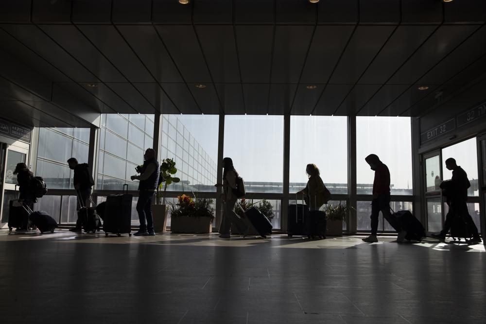FILE – Travelers walk with their luggage in the Ben Gurion Airport near Tel Aviv, Israel, Sunday, Nov. 28, 2021. Israeli ministers on Monday agreed to ban travel to the United States, Canada and eight other countries amid the rapid, global spread of the omicron variant. (AP Photo/Ariel Schalit, File)