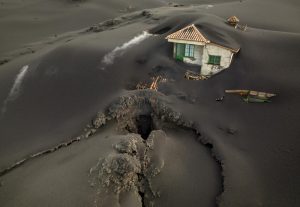 FILE – A fissure is seen next to a house covered with ash on the Canary island of La Palma, Spain, Dec. 1 2021. Authorities on a Spanish island are declaring a volcanic eruption that has caused widespread damage but no casualties officially finished, following ten days of no significant sulfur dioxide emissions, lava flows or seismic activity. But the emergency in La Palma, the northwesternmost of the Atlantic Ocean’s Canary Islands, is not over yet, said the director of the archipelago’s volcanic emergency committee, or Pevolca, Julio Pérez. (AP Photo/Emilio Morenatti, File)
