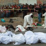 Bodies in bodybags are placed on the side of the road after an accident in Tuxtla Gutierrez, Chiapas state, Mexico, Dec. 9, 2021. Mexican authorities say at least 49 people were killed and dozens more injured when a cargo truck carrying Central American migrants rolled over on a highway in southern Mexico. (AP Photo )