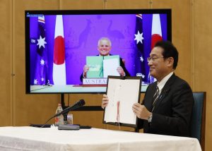 Japan’s Prime Minister Fumio Kishida, right, and Australia’s Prime Minister Scott Morrison, seen on screen, show off signed documents during a virtual summit to sign the Reciprocal Access Agreement, at Kishida’s official residence in Tokyo, Japan Thursday, Jan. 6, 2022. The leaders of Japan and Australia signed a “landmark” defense agreement Thursday that allows closer cooperation between their militaries and stands as a rebuke to China’s growing assertiveness in the Indo-Pacific region. (Issei Kato/Pool Photo via AP)