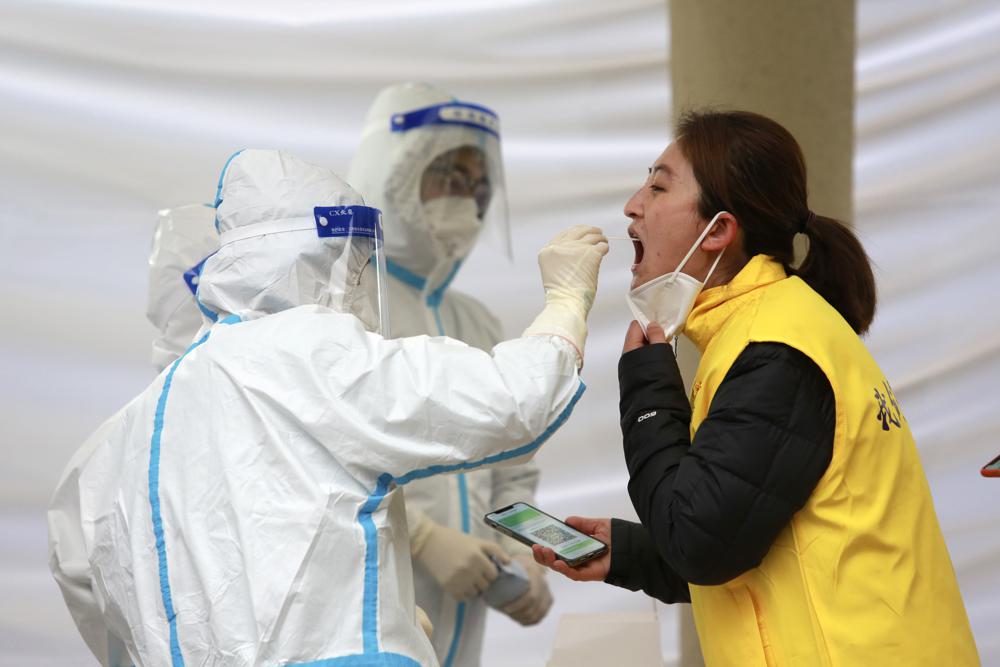 Workers wearing protective suits take a sample from a woman for a COVID-19 test in Xi’an in northwestern China’s Shaanxi Province, Tuesday, Jan. 4, 2022. Hospital officials in the northern Chinese city of Xi’an have been punished after a pregnant woman miscarried after being refused entry, reportedly for not having current COVID-19 test results. (Chinatopix via AP)