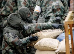 File photo of police dressed in military gas masks and chemical resistant suits loading bags of …