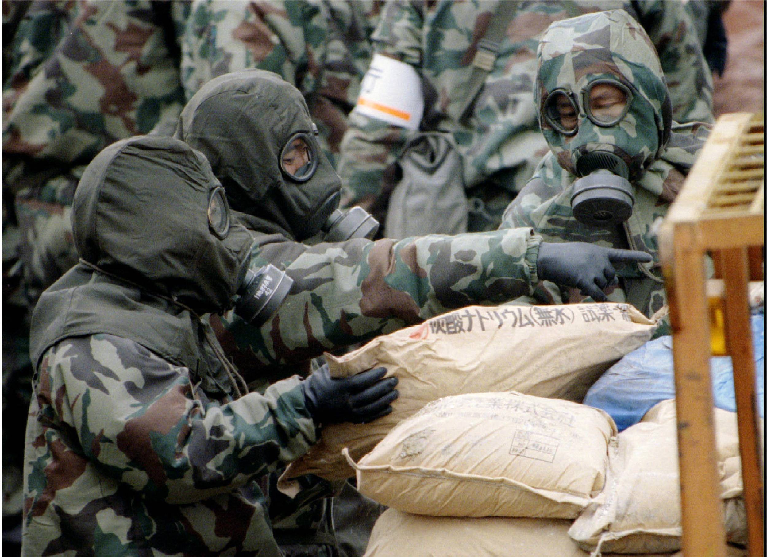 File photo of police dressed in military gas masks and chemical resistant suits loading bags of …