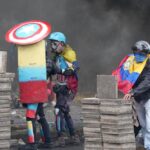 Protesters take cover during clashes with police in downtown Quito, Ecuador, Friday, June 24, 2022. The protesters are part of a national strike that the Confederation of Indigenous Nationalities began June 14 to demand that gasoline prices be cut, price controls for agricultural products and a larger budget for education.(AP Photo/Dolores Ochoa)