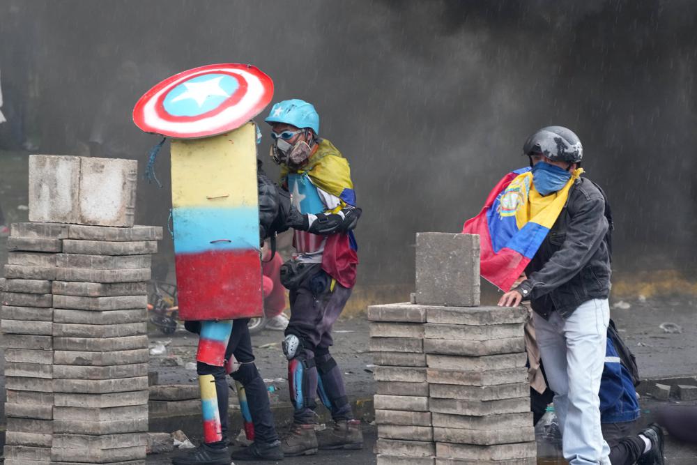 Protesters take cover during clashes with police in downtown Quito, Ecuador, Friday, June 24, 2022. The protesters are part of a national strike that the Confederation of Indigenous Nationalities began June 14 to demand that gasoline prices be cut, price controls for agricultural products and a larger budget for education.(AP Photo/Dolores Ochoa)