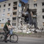 A man rides a bicycle past a building damaged in Russian shelling in Bakhmut, Donetsk region, Ukraine, Monday, June 20, 2022. (AP Photo/Efrem Lukatsky)