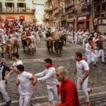 People run through the streets with fighting bulls and steers during the last day of the running of the bulls at the San Fermin festival in Pamplona, northern Spain, Thursday, July 14, 2022. (AP Photo/Alvaro Barrientos)