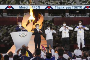 FILE – International Olympic Committee’s President Thomas Bach and Seiko Hashimoto, president of the Tokyo Organizing Committee of the Olympic and Paralympic Games make the sign of a heart with their hands during the closing ceremony in the Olympic Stadium at the 2020 Summer Olympics, Sunday, Aug. 8, 2021, in Tokyo, Japan. The Tokyo Olympics survived the COVID-19 postponement, soaring expenses and some public opposition. A year later, the costs and benefits are as difficult to untangle as the Games were to pull off. (Dan Mullen/Pool Photo via AP)