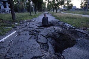 FILE – Viktor Shevchenko stands in a crater to show its depth after a Russian attack in the Saltivka district in Kharkiv, Ukraine, July 1, 2022. As Russia’s invasion of Ukraine grinds into its fifth month, some residents close to the front lines remain in shattered and nearly abandoned neighborhoods. One such place is Kharkiv’s neighborhood of Saltivka, once home to about half a million people. Only perhaps dozens live there now, in apartment blocks with no running water and little electricity. (AP Photo/Evgeniy Maloletka, File)