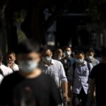 Commuters wearing face masks walk along a street in the central business district in Beijing, Thursday, July 7, 2022. (AP Photo/Mark Schiefelbein)